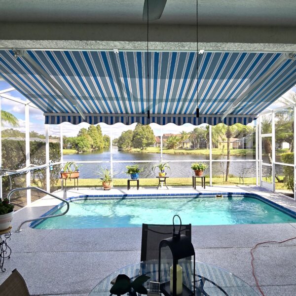 Custom blue and white striped retractable awning installed inside a screened pool enclosure with lakefront view in Tampa Bay, Florida by Cover Up Awning Company