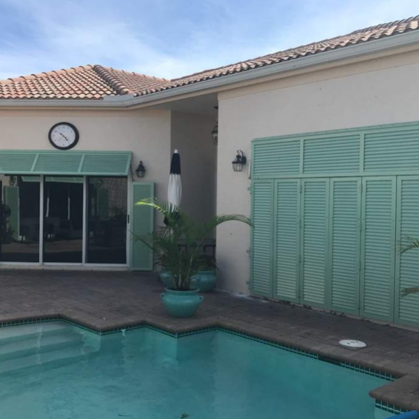 Custom green Bahama shutters and decorative shutter panels installed on a luxury Florida pool home, providing shade, privacy, and coastal style.