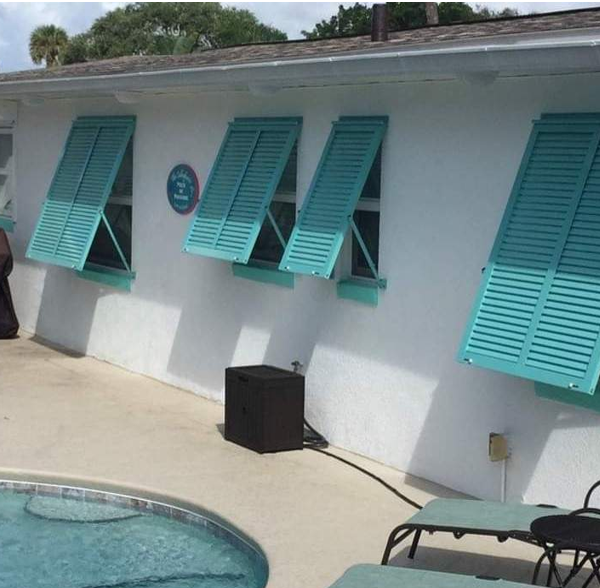 Turquoise Bahama shutters installed on poolside windows of a Florida home, providing shade, privacy, and tropical curb appeal.