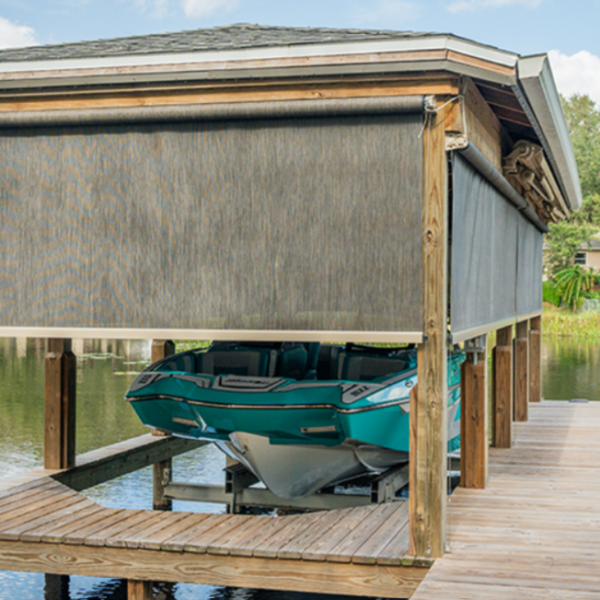 Motorized screens installed around a waterfront boat dock, providing shade, privacy, and protection for a covered boat lift and dock area.